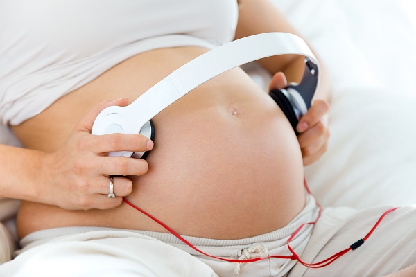 Portrait of pregnant woman putting headphones on her belly.